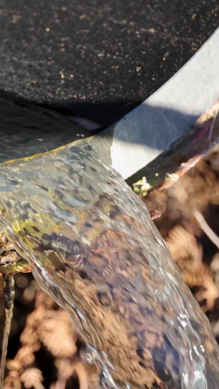 Um fluxo constante de água límpida jorra de um cano de metal sobre solo seco.