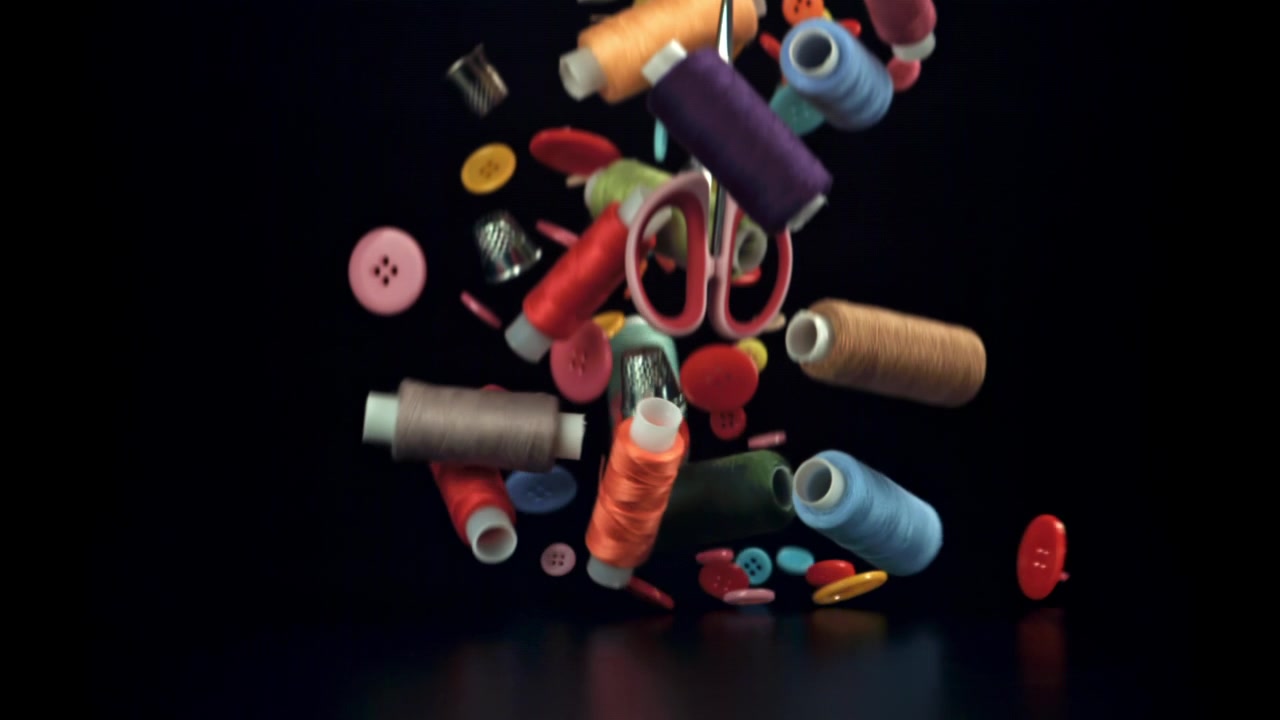 Slow motion of colorful sewing supplies falling onto a black surface