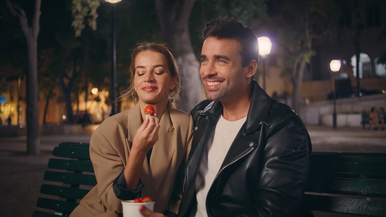 Relaxed partners eating strawberry in city park. Beautiful girl enjoying date