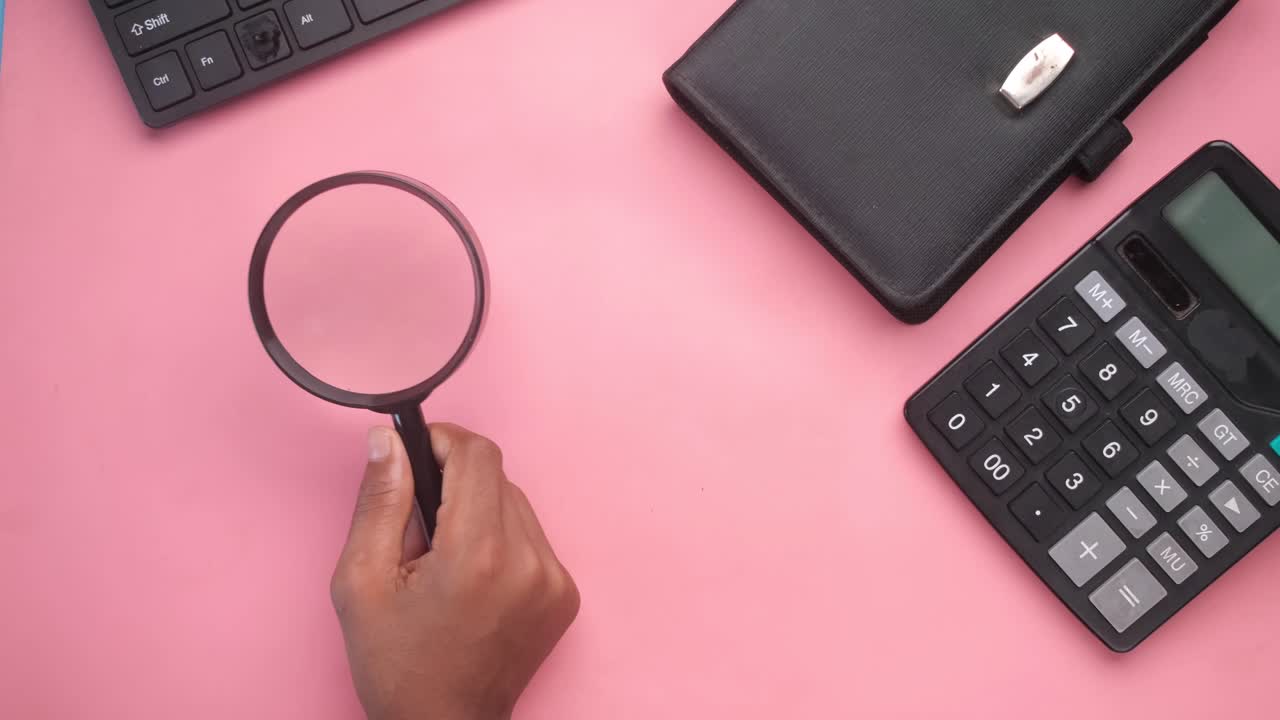 persona que usa una lupa en un escritorio rosado con suministros de oficina