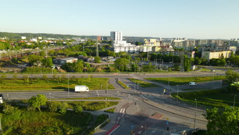 Flying-back-over-Complicated-Road-Intersection,-cargo-train-moving-along-railway-and-Gdansk-city-panorama-on-sunny-day-Poland