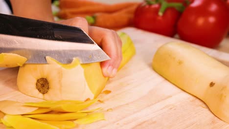 hands peeling squash with knife on cutting board