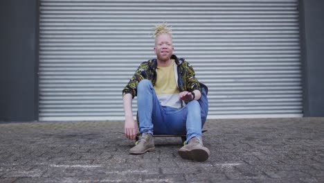 retrato de un hombre afroamericano albino sonriente sentado en un monopatín mirando a la cámara