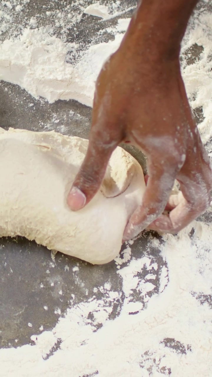 Video verticale: Mani infarinate che premono e modellano l'impasto al bancone della panetteria, mostrando un orologio da polso.