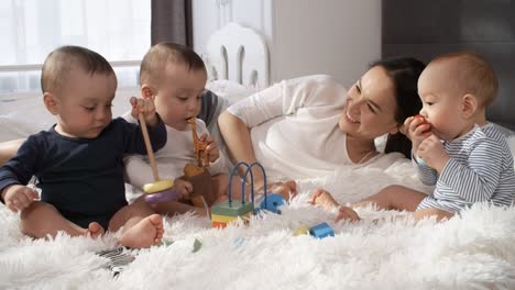 mutter liegt auf flauschiger tagesdecke im schlafzimmer und spielt mit ihren drei kindern