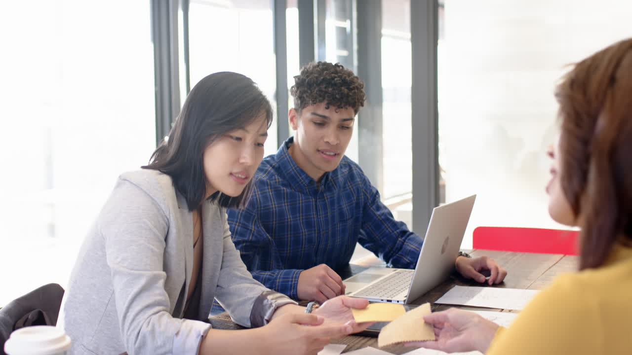 Collaborating on project details, multiracial colleagues using laptop and documents in office