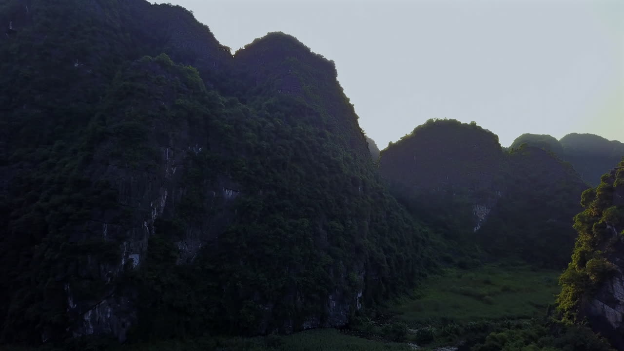 Witness a breathtaking sunrise in Ninh Binh, Vietnam, as golden rays of light pierce through the majestic rock formations, creating a stunning and serene landscape