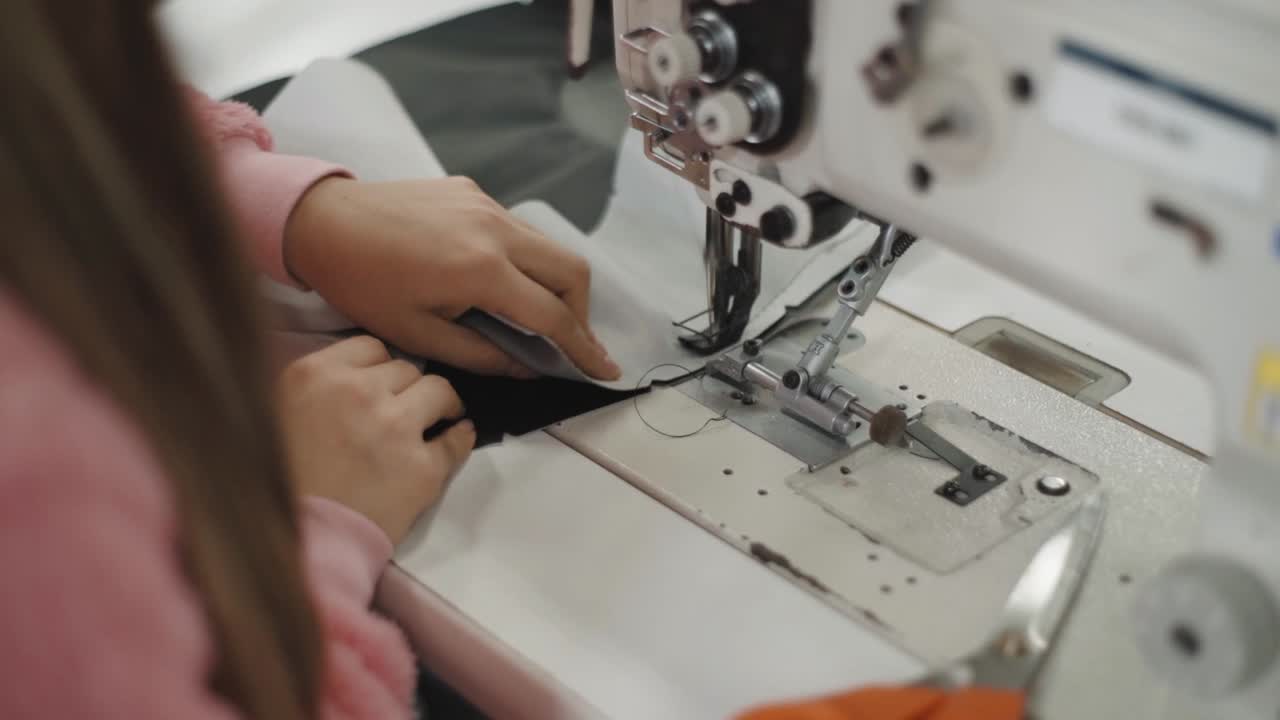 Shot of a female workers hands feeding fabric into an industrial sewing machine, inside workshop.