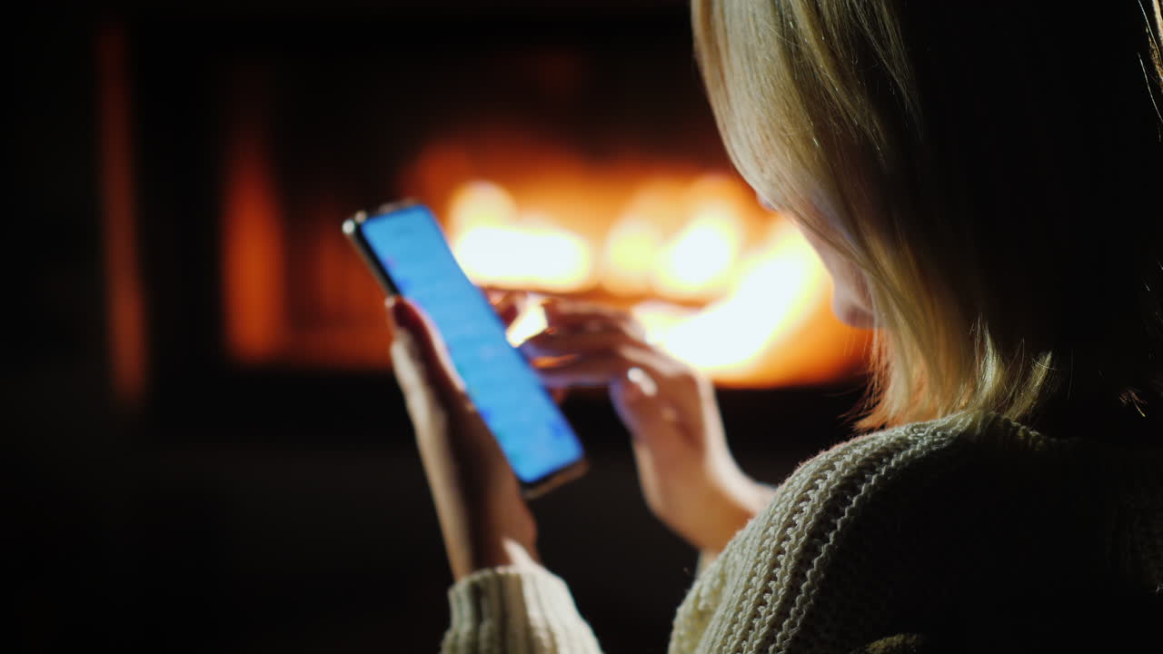 eine frau benutzt abends ein smartphone am kamin