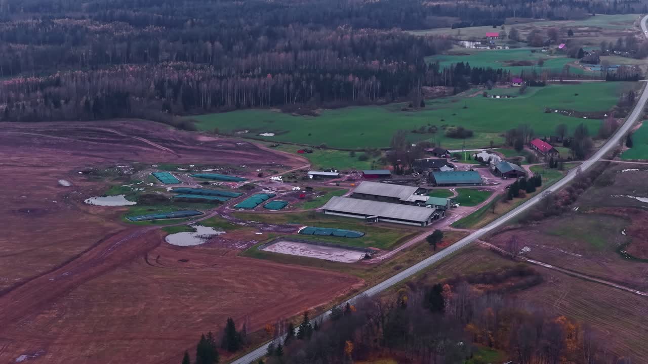 Aerial panorama of countryside in Latvia with large open farmlands and small forest, reveals campground cabins for gathering near water