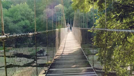 male tourist walks on suspension rope bridge in the forest and taking photos at scenery