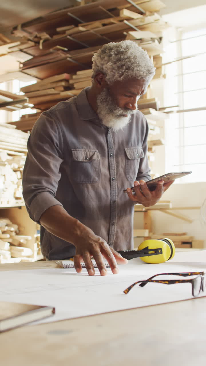 video vertical de un carpintero afroamericano de edad avanzada usando una tableta en el taller