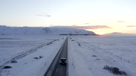 AERIAL:-Snow-White-Landscape-with-Road-following-Car-in-Iceland-Winter,-Sunset,-Arctic