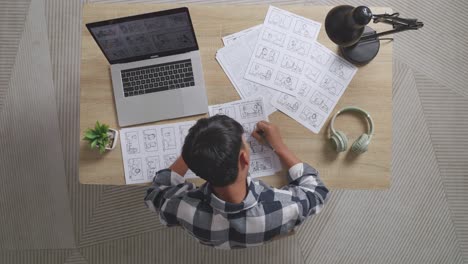 vista superior de artista masculino asiático pensando en dibujar concepto luego levantando su dedo índice mientras dibuja storyboard en la mesa con una computadora portátil y auriculares en el estudio