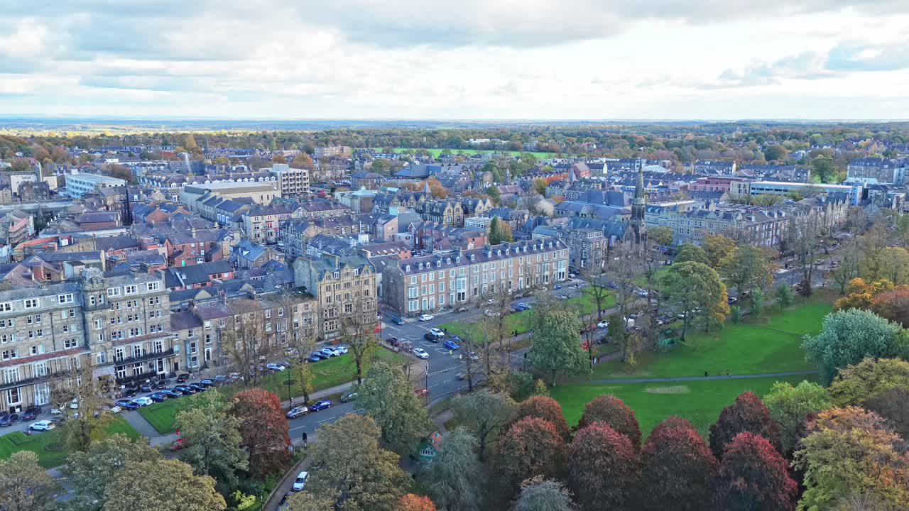 Ascending aerial shot over Harrogate, North Yorkshire, showcases historic town centre with elegant Victorian terraced blocks, and the iconic open parkland of The Stray in autumn hues