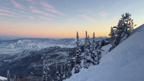 tilt up shot of a stunning winter landscape scene looking down at a cloudy snow covered valley during a golden sunset from the summit of a ski resort in the rocky mountains of utah