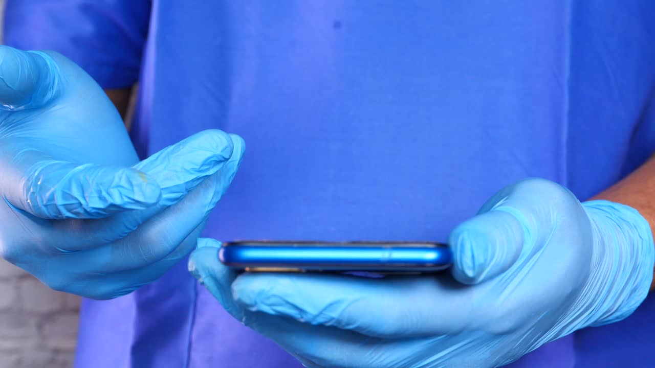 médico usando un teléfono inteligente con guantes médicos azules