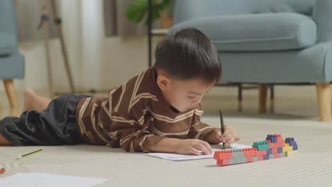 close up of asian kid lying on the floor in the room with plastic toy brick drawing at home