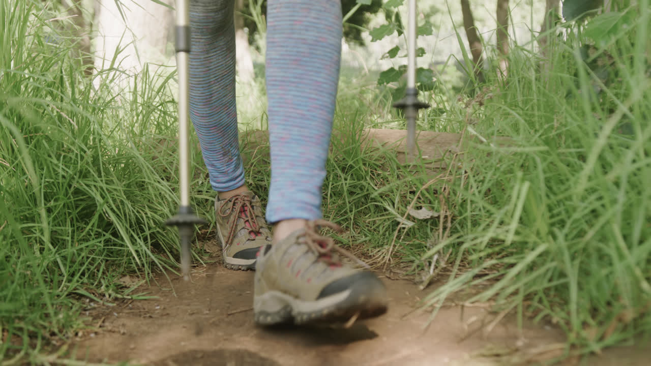 Low section of african american woman hiking with trekking poles in forest, slow motion