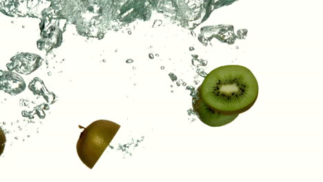 trozos de kiwi sumergiéndose en el agua sobre un fondo blanco