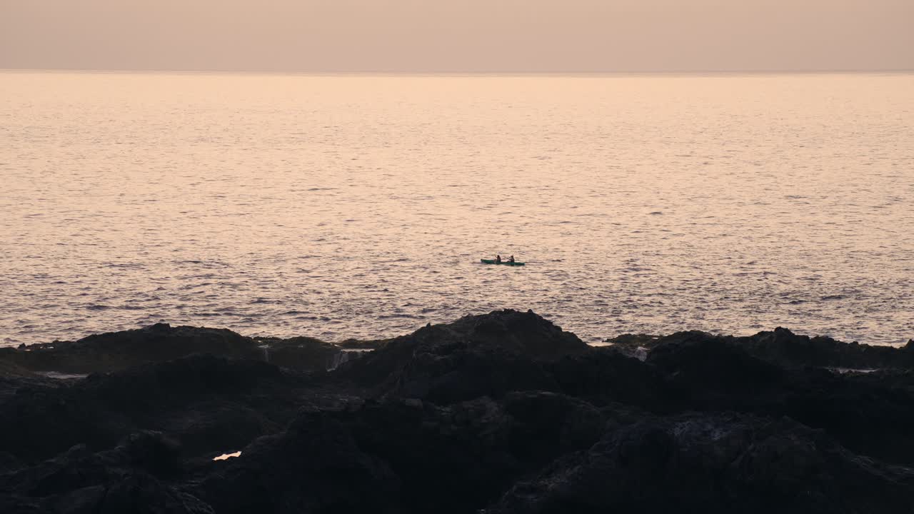 Silhouetted kayakers paddle in the ocean, bathed in the golden backlight