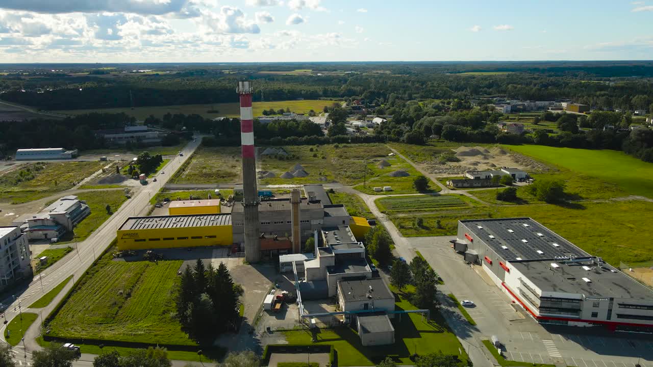 Aerial drone video orbiting and flying around a tall smoke stack chimney factory pipe industrial tower with communication technology mounted on top of it during a sunny day in a small industrial town