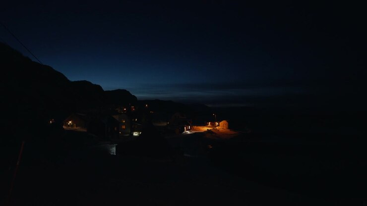 Villaggio costiero della Norvegia artica all'ora blu con luci brillanti sotto scure sagome montuose