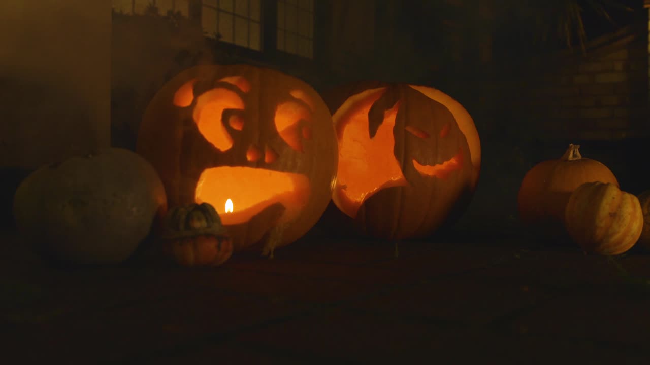 2 calabazas iluminadas talladas fuera del frente de una casa halloween con humo con pequeñas calabazas