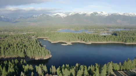 Panorámica-Aérea-De-Una-Cordillera-Cubierta-De-Nieve-Y-Un-Hermoso-Valle-De-árboles-De-Hoja-Perenne