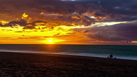 Zeitrafferaufnahme-Von-Menschen-Am-Strand,-Die-Den-Wunderschönen-Goldenen-Sonnenuntergang-Zwischen-Wolken-über-Dem-Meer-Genießen
