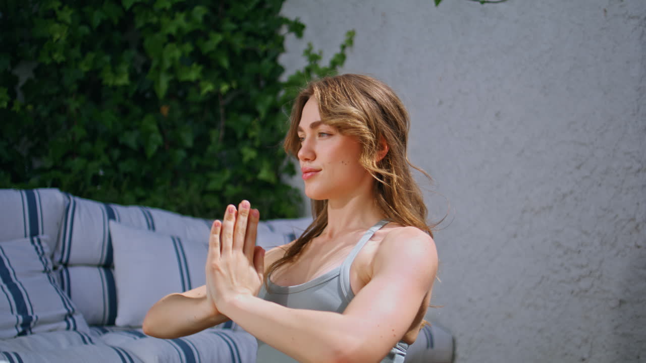 Woman athlete stretching arms overhead making yoga pose on sunny patio closeup
