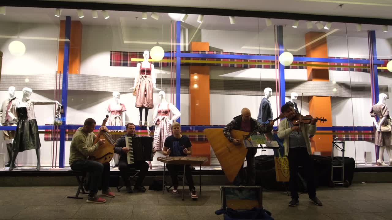 Street musicians perform in Munich, Germany, at night, playing for passersby and hoping for donations, as people stroll through the vibrant city streets.