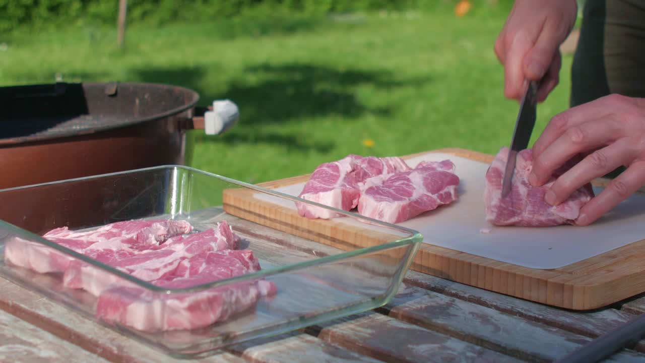 Male hands slice pork meat with chef&acute;s knife by the grill in home garden