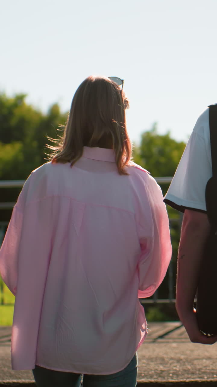 밝은 빛 아래에서 야외 계단을 고, 따뜻하게 상호 작용하고, 배을 들고, 초록색과 현대적인 구조물과 함께 뒷면으로 보이는 친구들의 뒷면