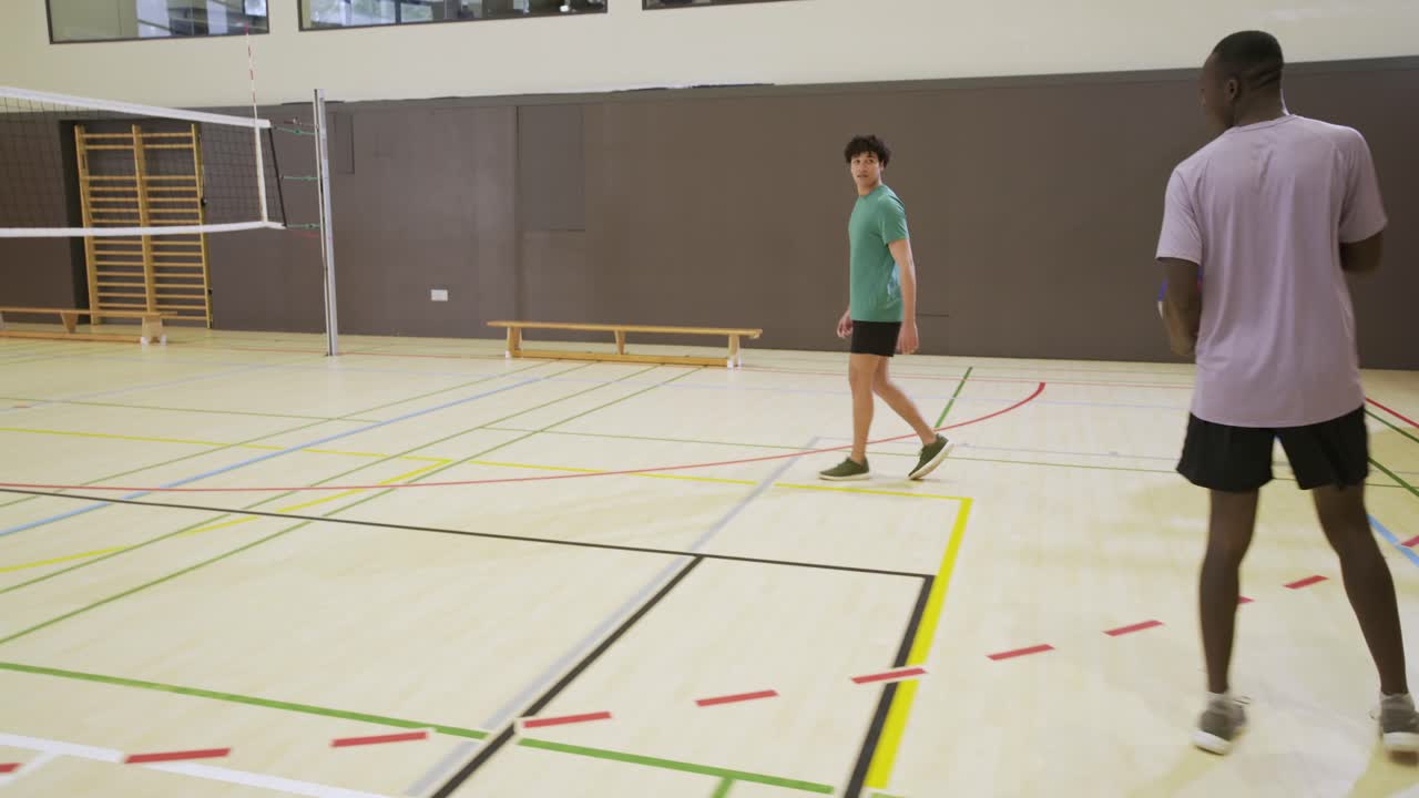 Homens diversos iniciando um rali de vôlei por diversão, sacando sobre a rede, passando e se movimentando no ginásio, com espaço para texto.
