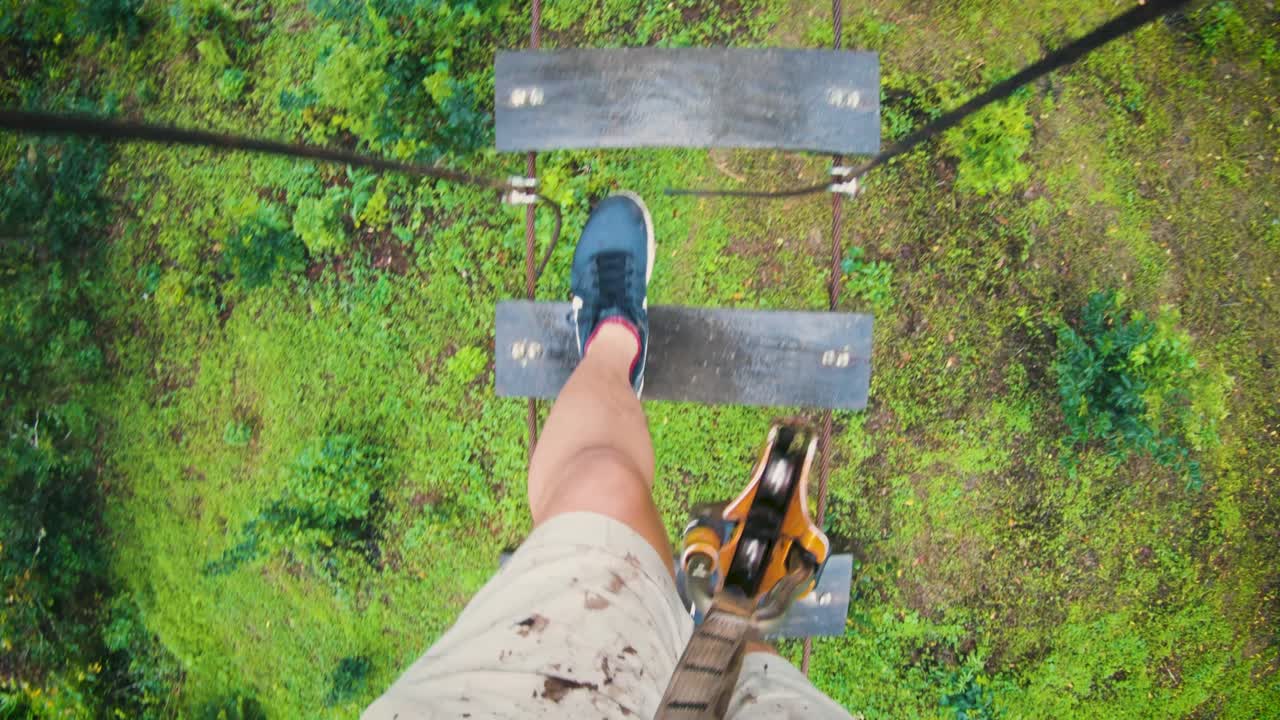 Ripresa POV di un uomo che cammina sull'ostacolo a corde alte con piccole assi di legno nella giungla lussureggiante a Chiang Mai, Thailandia - ripresa dall'alto