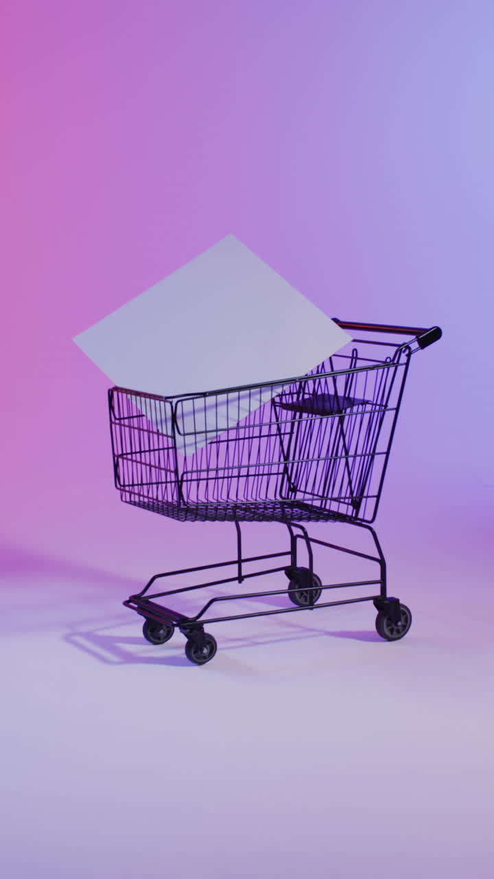 Vertical video of shopping trolley with white canvas with copy space over pink neon background