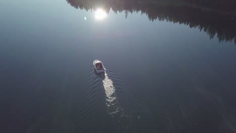 Beautiful-aerial-view-of-family-in-a-boat-moving-slowly-through-Norwegian-fjord-with-lull-water-reflecting-the-sunlight-and-islands,-Camera-tilting-up-to-reveal-the-summer-archipelago-of-Scandinavia