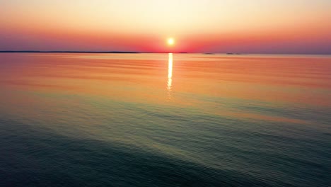 Hermoso-Amanecer-En-El-Océano-Con-Un-Sol-Brillante-Que-Proyecta-Coloridos-Reflejos-Rojos,-Naranjas,-Morados-Y-Amarillos-Sobre-Las-Tranquilas-Olas-Del-Mar