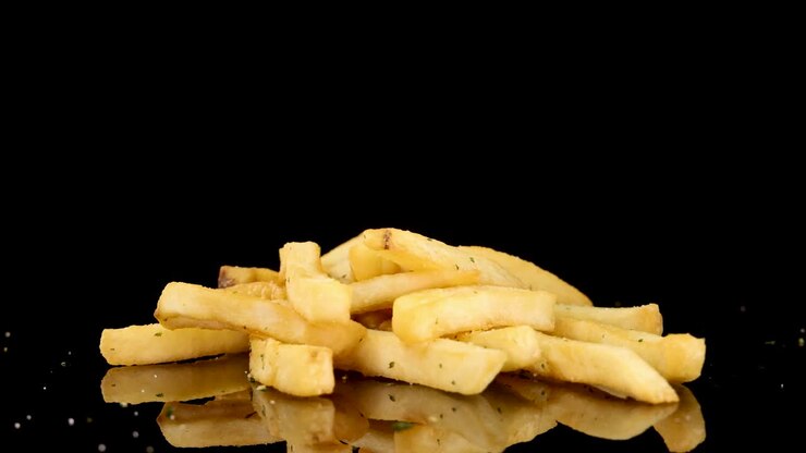 Golden French fries rotate smoothly on a reflective black surface, illuminated by studio lighting. The camera maintains a consistent angle, emphasizing texture and seasoning