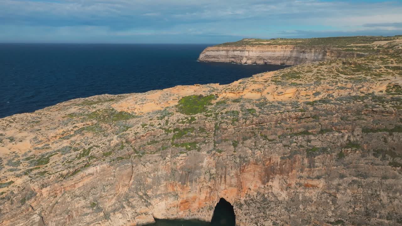 A stunning cinematic aerial reveal of the Dwejra Inland Sea in Gozo, featuring a natural sea cave tunnel through massive limestone cliffs. Captures the authentic Mediterranean landscape