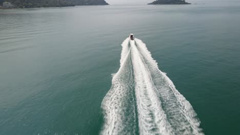 aerial drone follow shot of a speed boat traveling fast towards an island in a tropical sea with mountain coastline