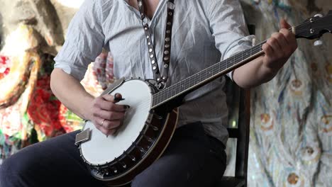 male musician playing banjo sitting chair indoor.