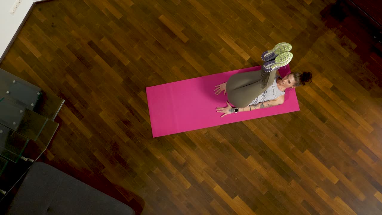 una mujer está haciendo abdominales inversos desde la perspectiva de un pájaro en una alfombra de yoga rosa