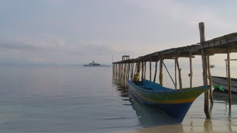 Small-wooden-boat-anchored-in-Indonesia-at-jetty-with-luxury-superyacht-in-background