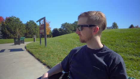 a man ends a phone call on a bench at a city park on a beautiful sunny day