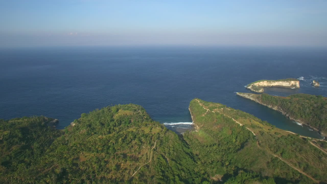 앞으로 날아가는 무인 항공기는 정글의 야자수 위 높은 황금 시간 푸른 바다에서 atuh 해변 근처에서 아래로 기울어집니다.