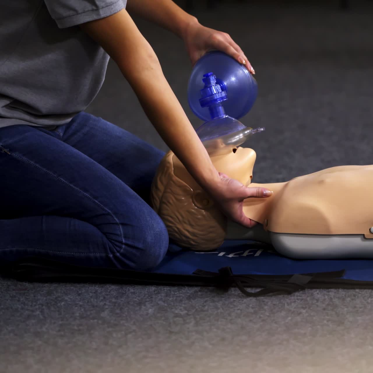 Instructor demonstrates breathing exercise on a mannequin. Woman on a mat on the floor over the dummy giving a medical training