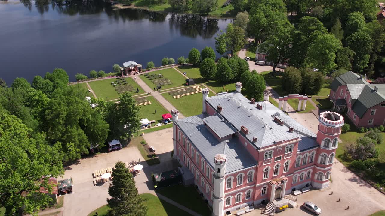 Aerial view of the small town of Birini Castle, located in a green park. The parish is surrounded by well-maintained paths, trees and open grass. Residential buildings and a lake