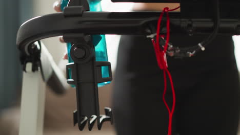 woman runs putting water bottle in holder closeup. energetic athletic woman hydrates during exercise routine at home slow motion. treadmill handles